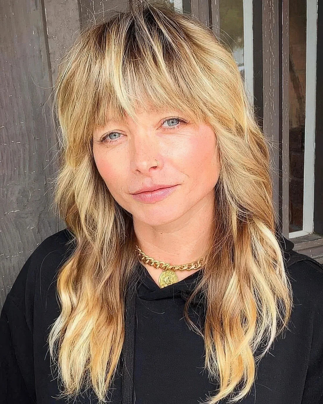 Long blonde wolf cut with outgrown blunt bangs and wavy volume.