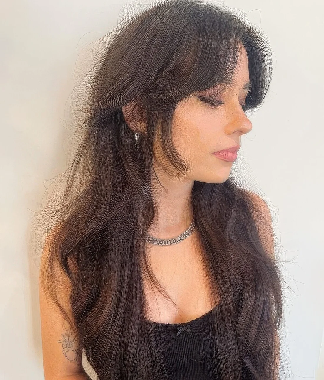 Dark brunette long wolf cut with curtain bangs, longer face-framing layers and wavy hair.