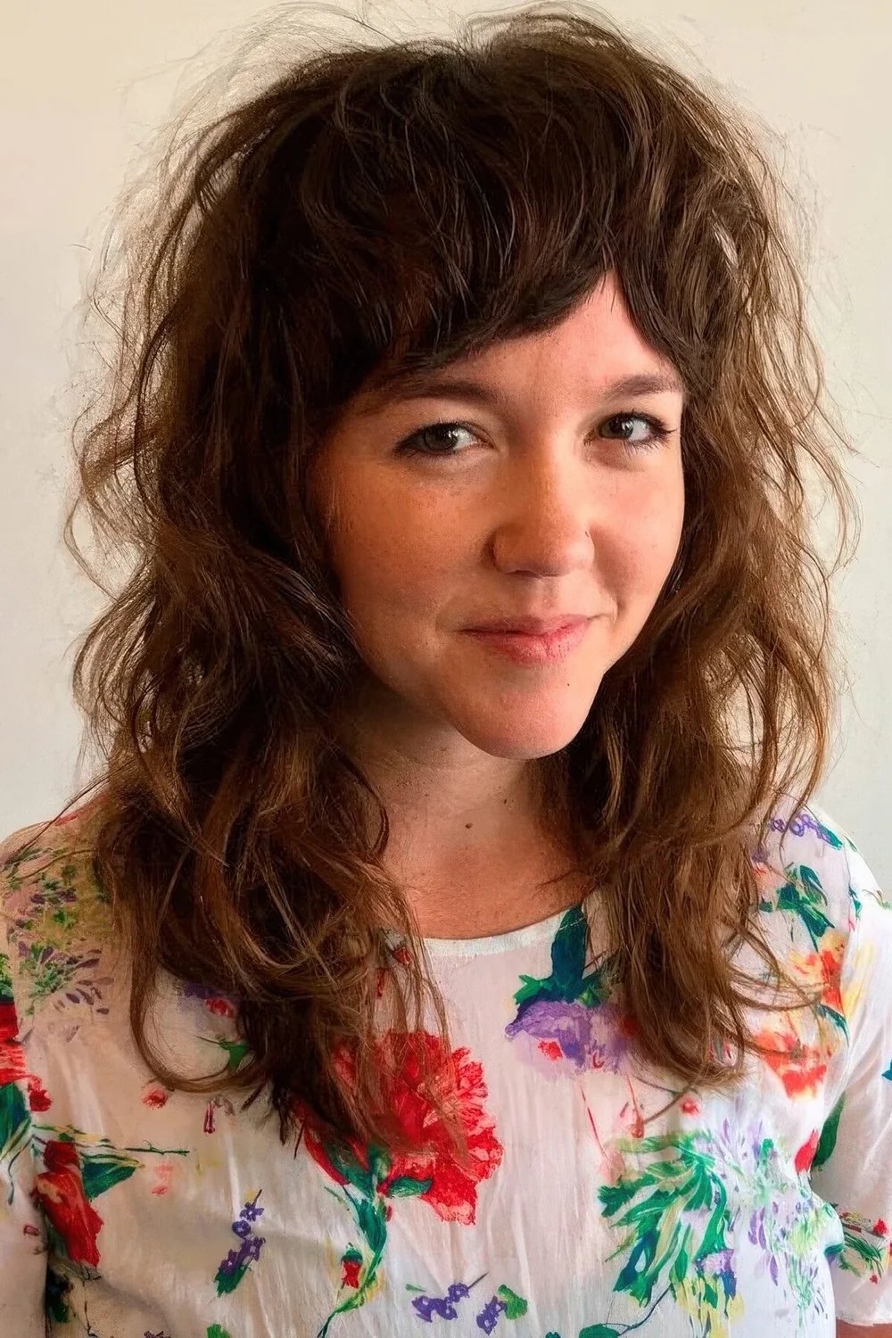 Voluminous wavy wolf cut with bottleneck bangs on naturally wavy hair.