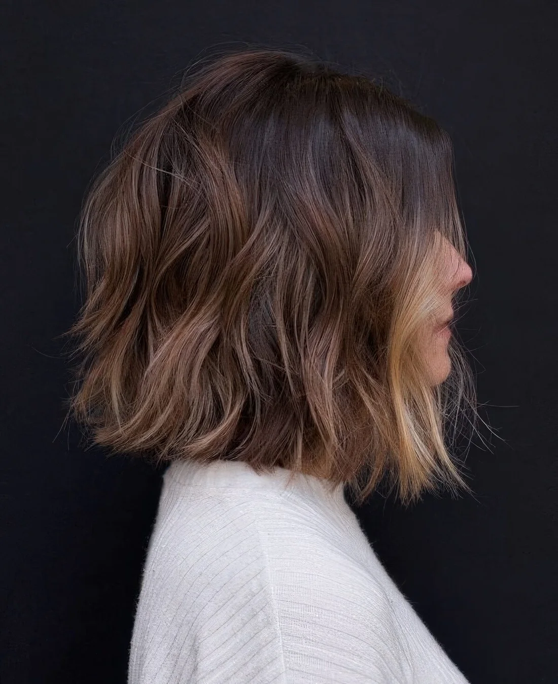 Dark brown bob with a black root, chestnut balayage and blonde money piece to highlight the look.