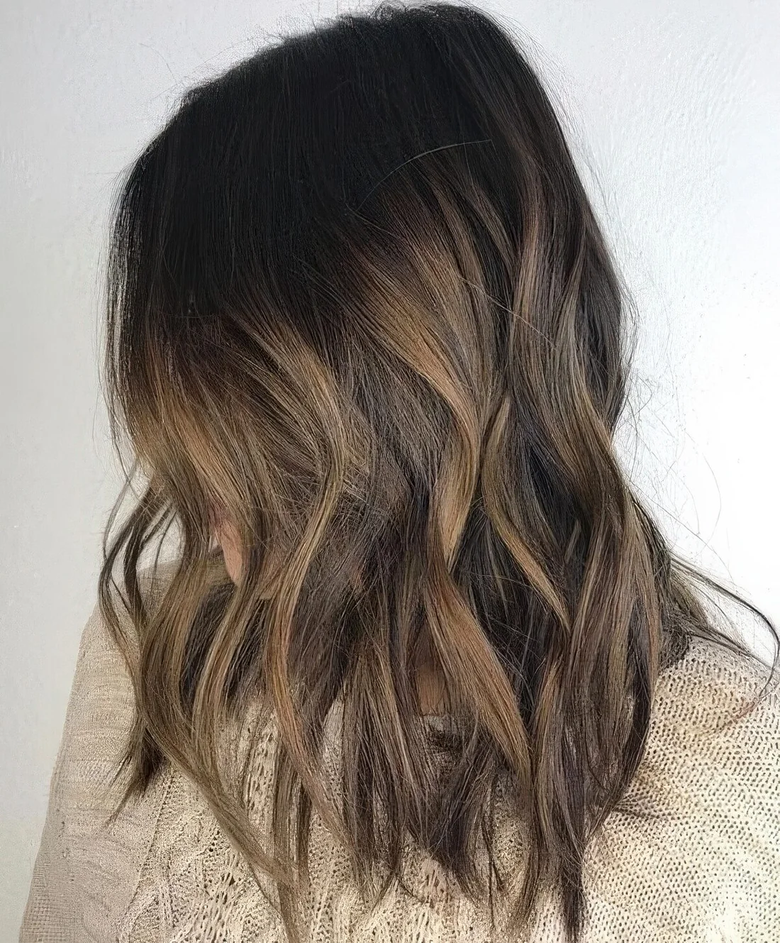Dark brunette hair with subtle bayalage highlights and medium-length.
