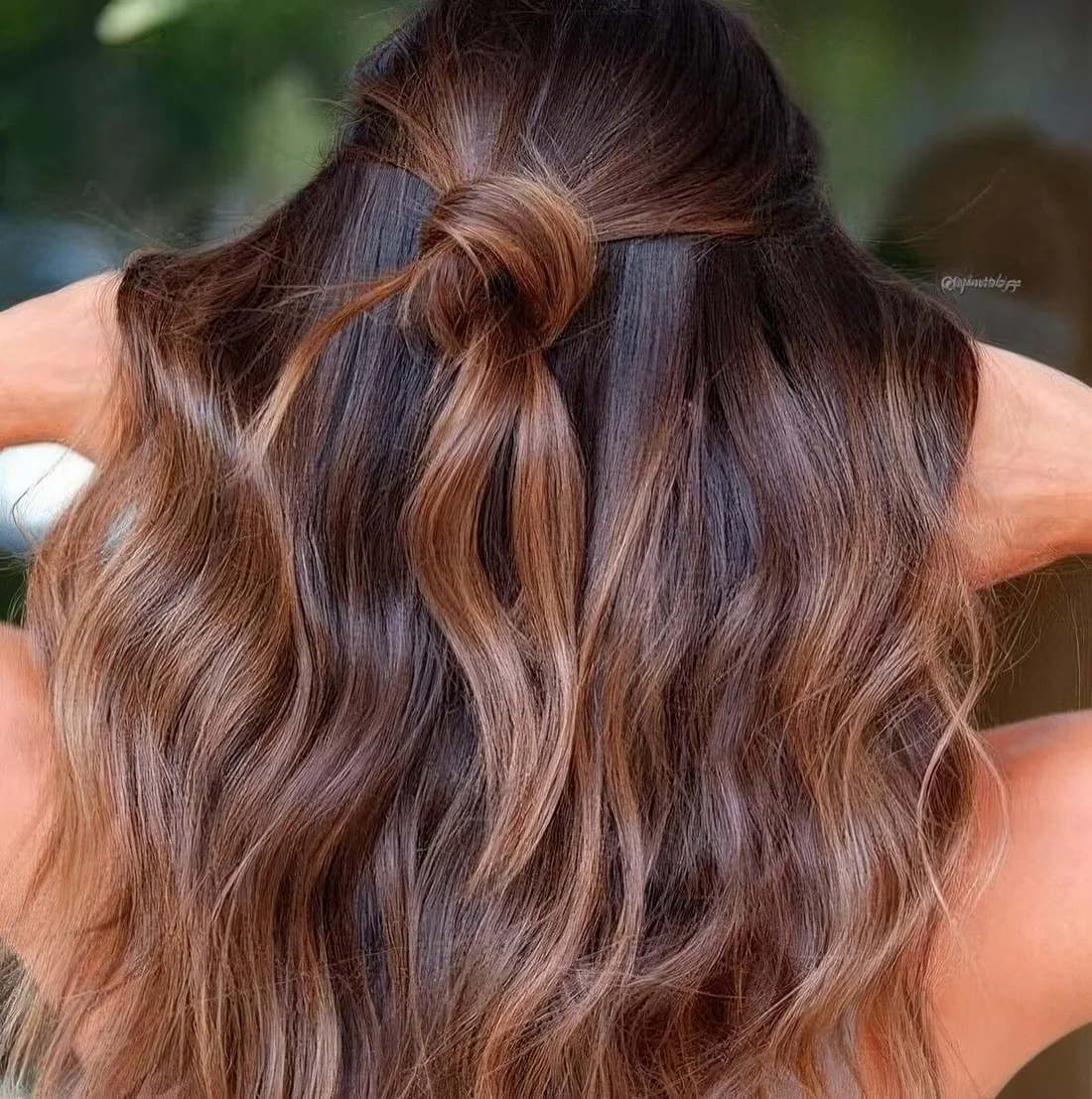 Dark chestnut hair with waves and a knot and with caramel balayage to give the hair more dimension and texture.