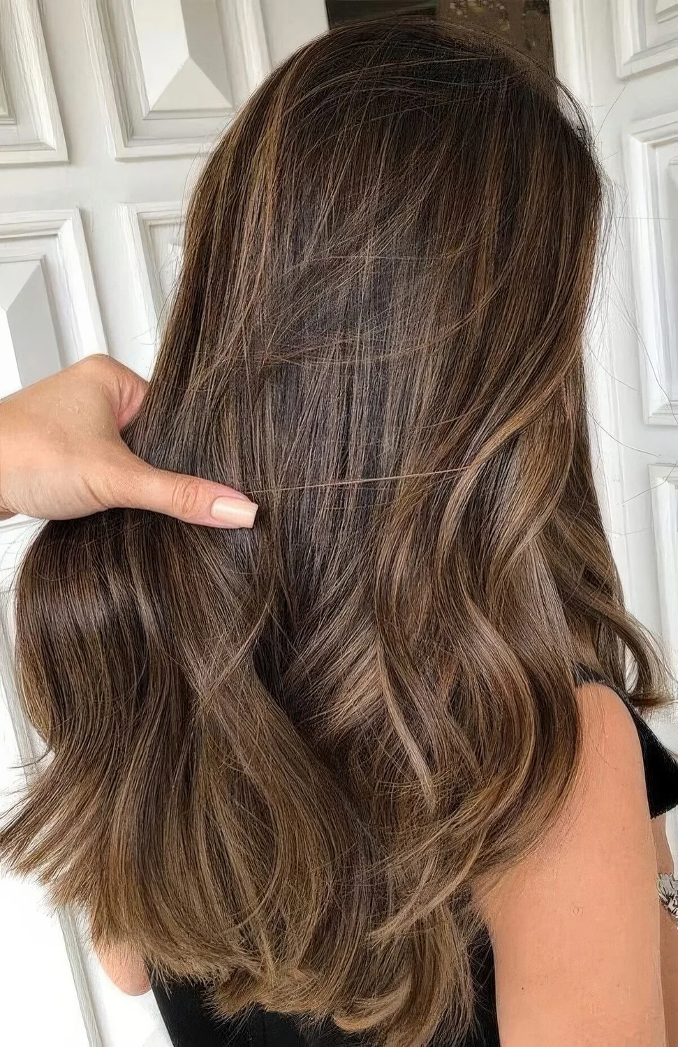 Long dark brown hair with delicate honey and caramel babylights that help long strands look dimensional and bold.