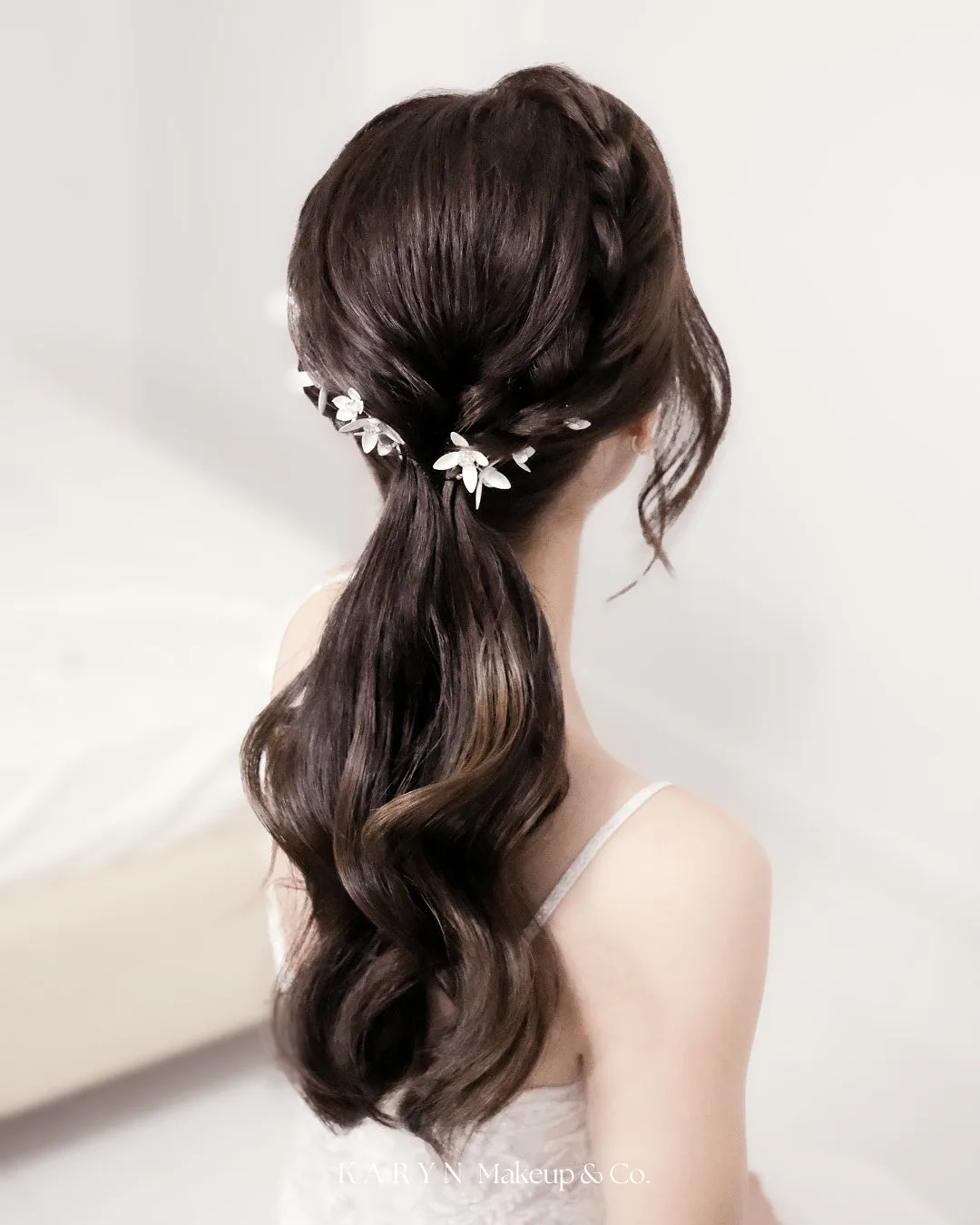 chest wavy brunette ponytail shown as a low ponytail hairstyles idea, featuring chest outline, shown in dark wavy low ponytail with floral pins