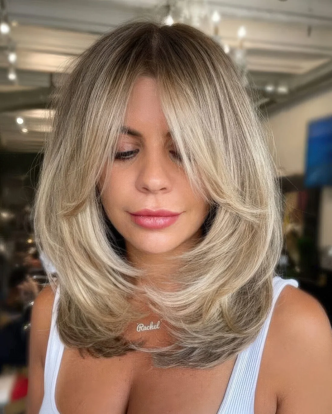 Chic blonde butterfly haircut of medium-length, with curtain bangs and wavy ends.