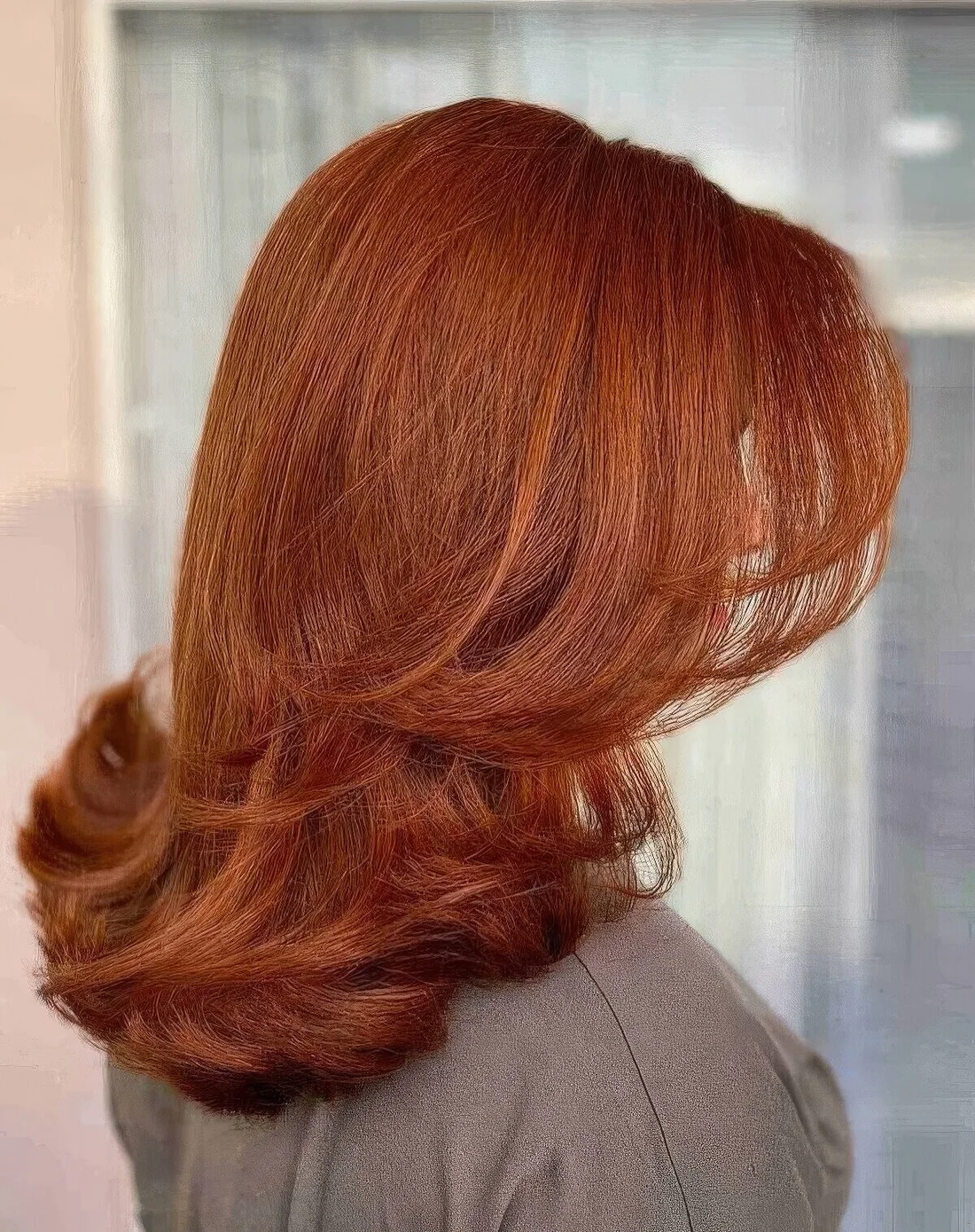 Bright copper butterfly haircut on medium-length hair, with curled ends.