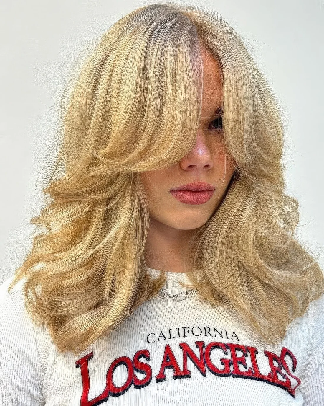 Fab blonde medium-length butterfly haircut with curtain bangs and curled ends.