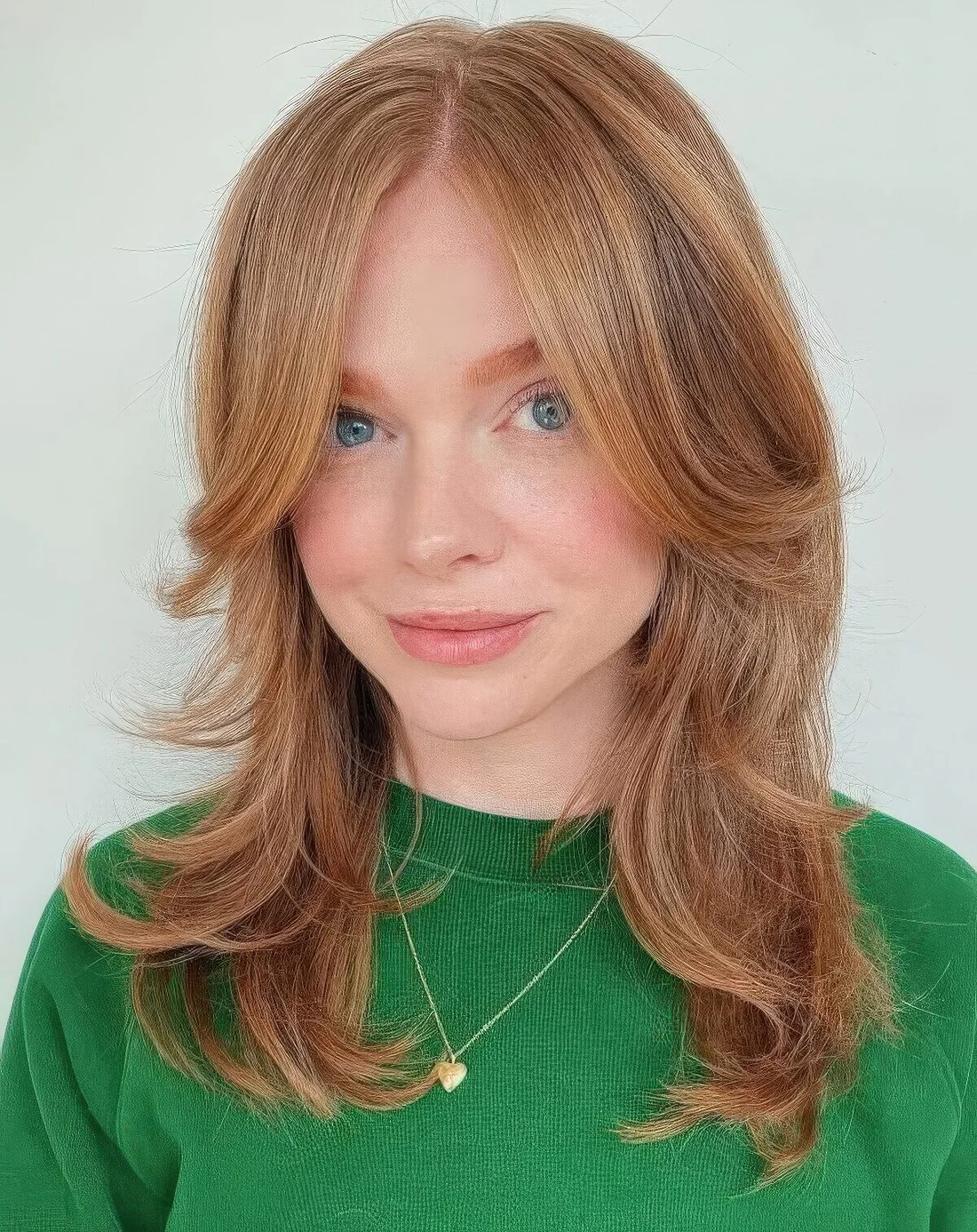 Ginger medium butterfly haircut with long curtain bangs and curled ends.