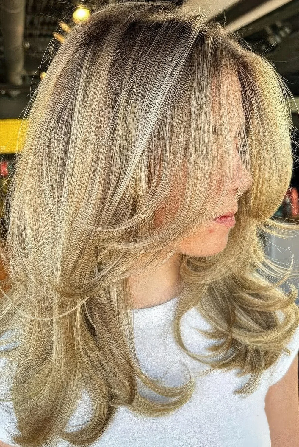 Medium-length blonde butterfly haircut with curled ends, a bit of volume and a darker root.