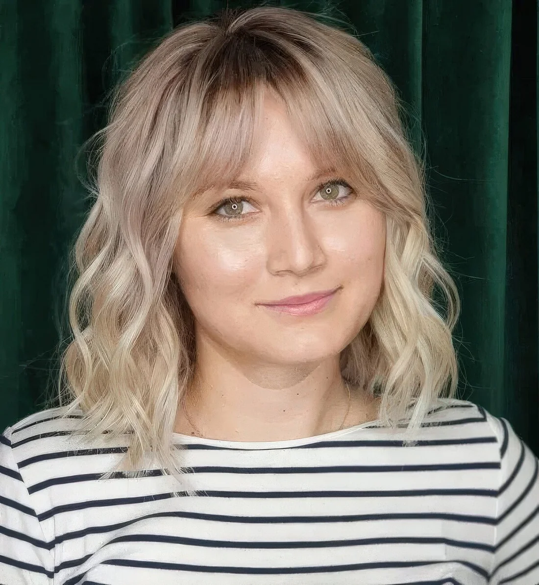 Blonde medium-length hairstyle with a darker root, bottleneck bangs and waves.
