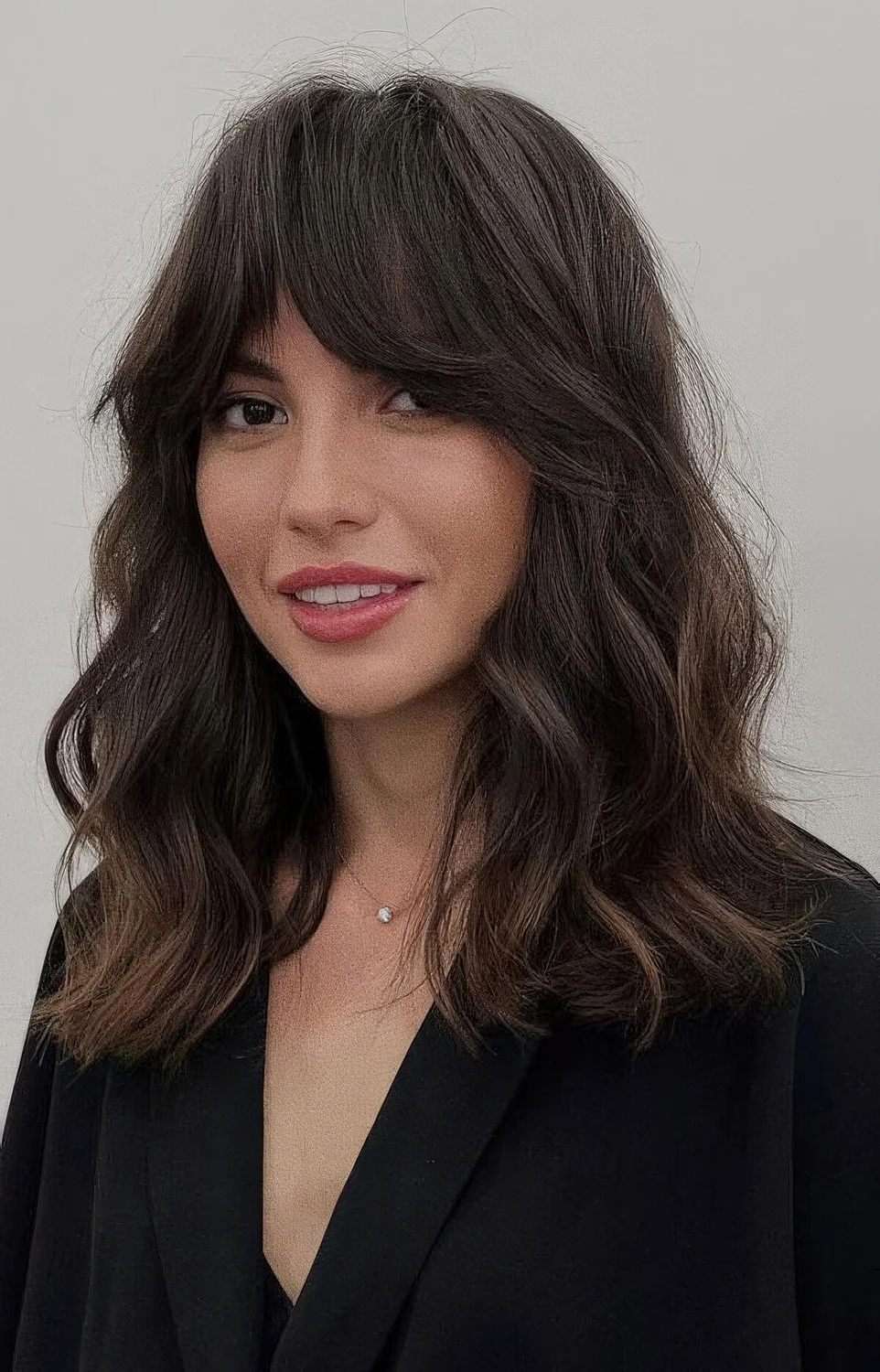 Dark brown medium-length haircut with bottleneck bangs and waves plus a lot of volume.