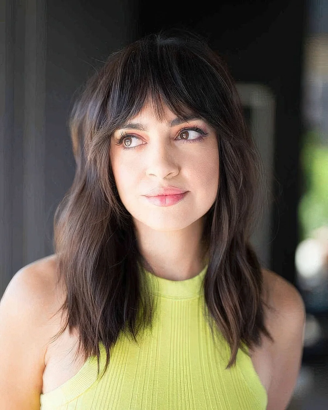Dark brunette wavy hairstyle with bottleneck bangs.