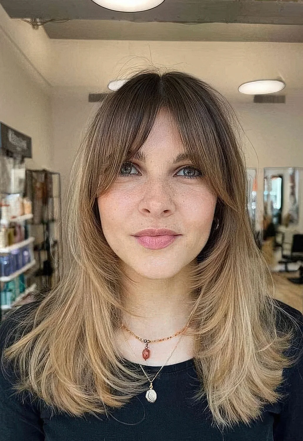 Medium blonde butterfly haircut with a darker root and front plus bottleneck bangs.