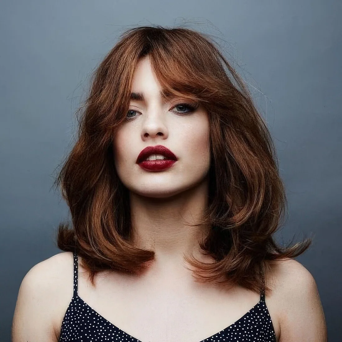 Auburn medium-length hair with waves and bottleneck bangs.