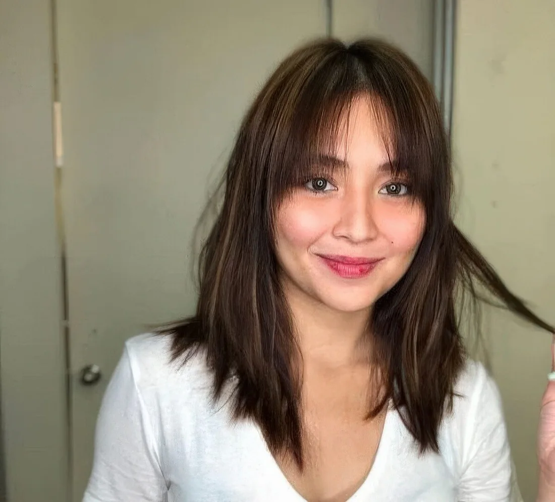 Dark brunette shoulder-length hair with bottleneck bangs and a bit of caramel highlights.