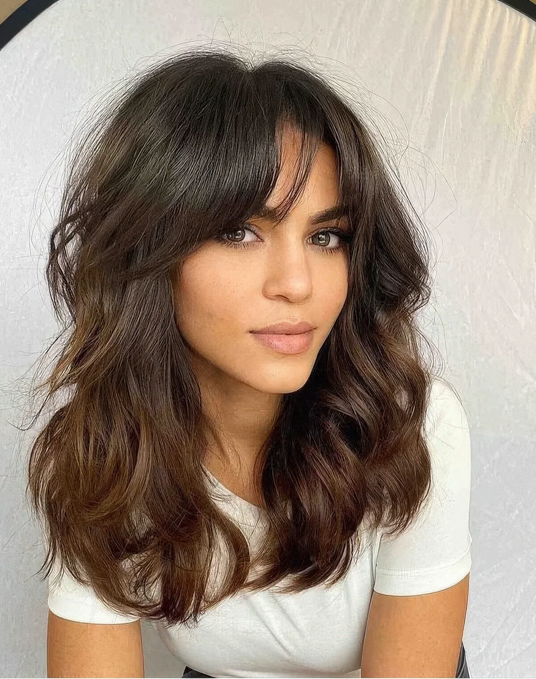 Medium-length dark chocolate hair with waves and texture and bottleneck bangs for a catchier look.