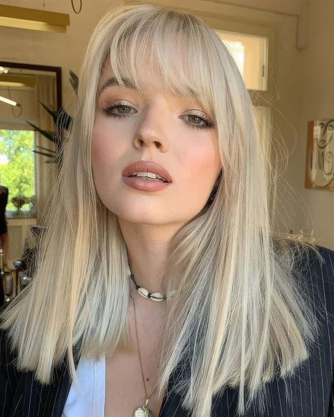 Straight creamy blonde medium-length hair with wispy bangs.