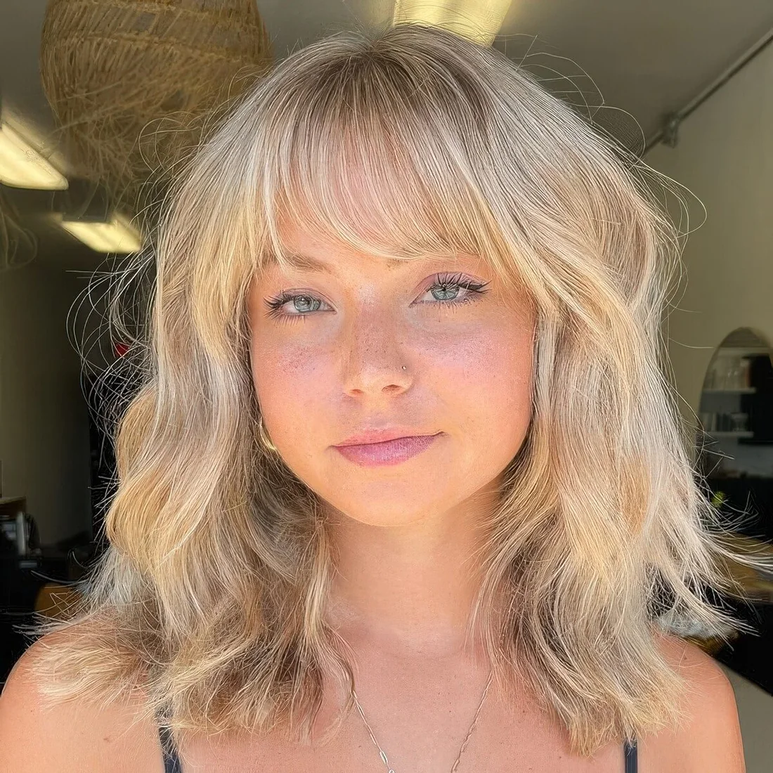 Thick wavy medium-length blonde hair with wispy bangs that take off some weight of hair from the front.