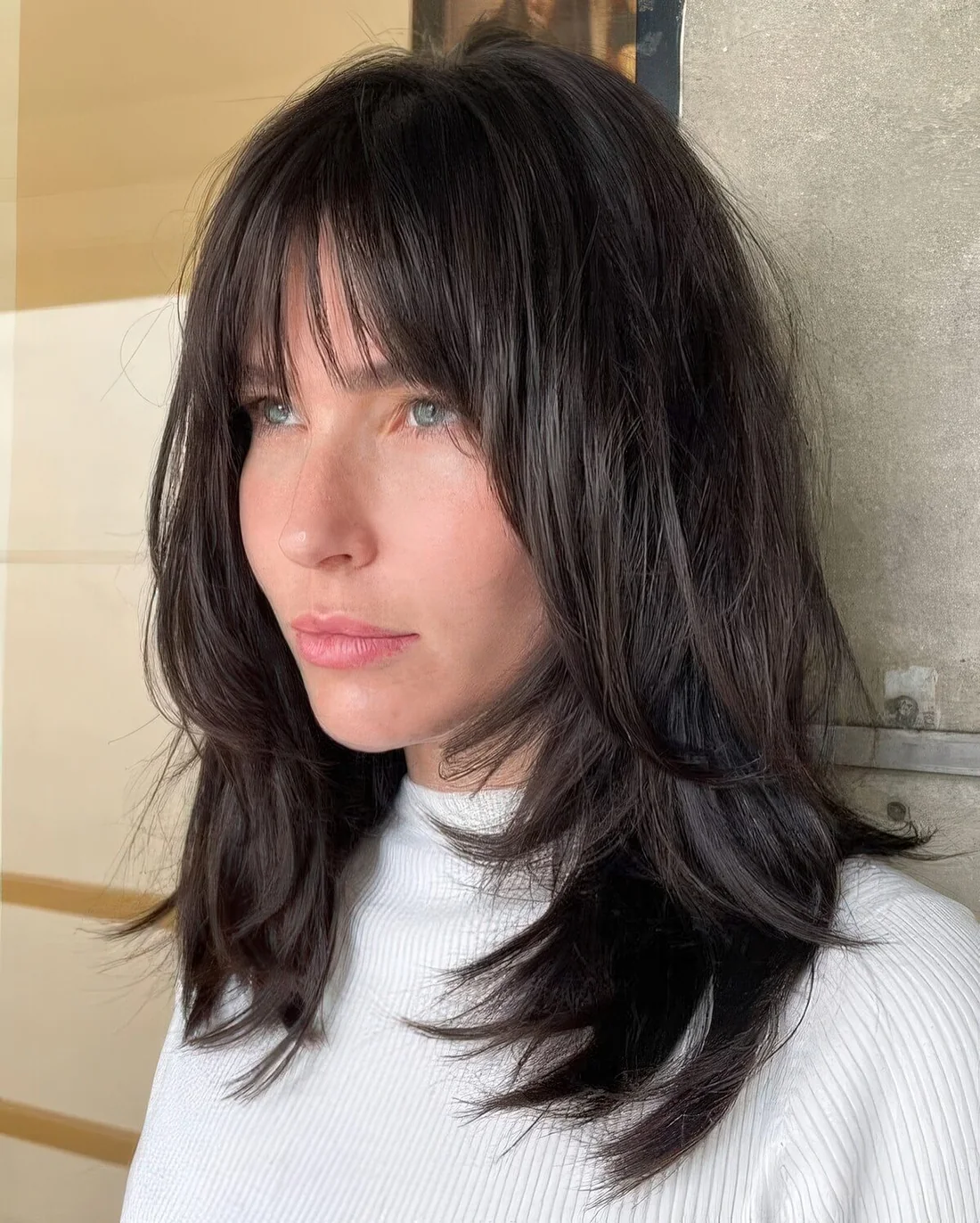 Dark brown medium-length hair with shaggy layers and wispy bangs.