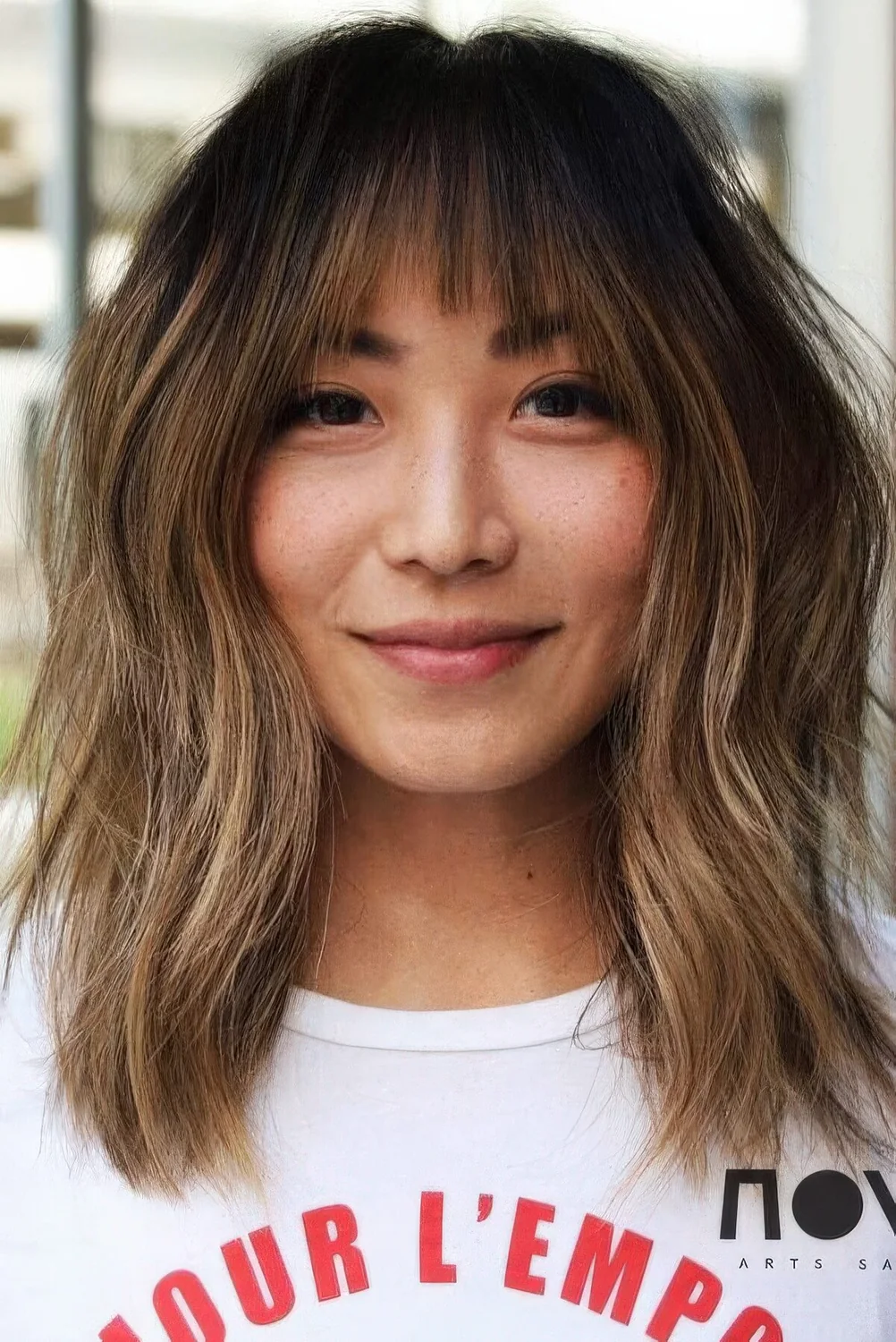Dark brunette medium-length hair with caramel balayage and ombre, wispy bangs and slight messy waves.