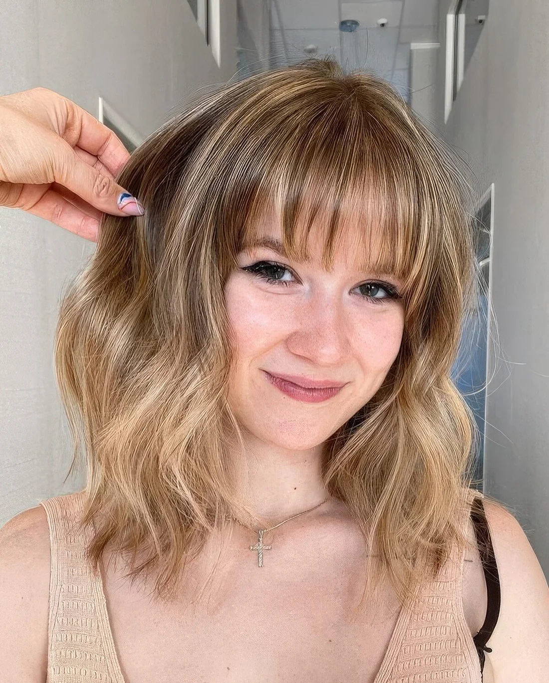 Medium-length bronde hair with blonde highlights and waves plus wispy bangs to accent the eyes.