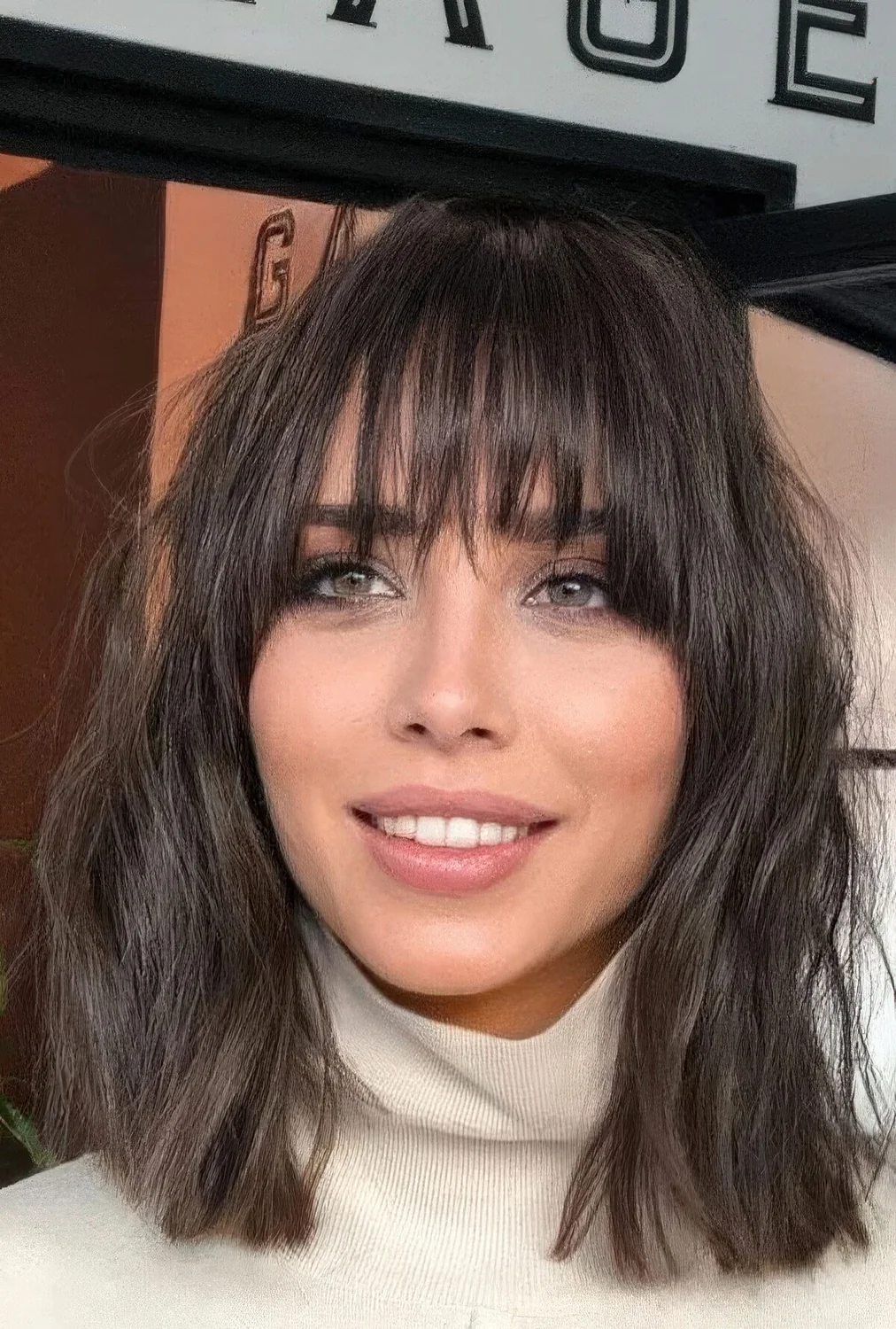 Medium-length brunette hair with waves and outgrown wispy bangs that give that effortless touch to the look.