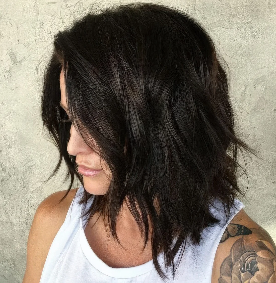 Black shaggy and choppy medium-length haircut with side part and messy waves.