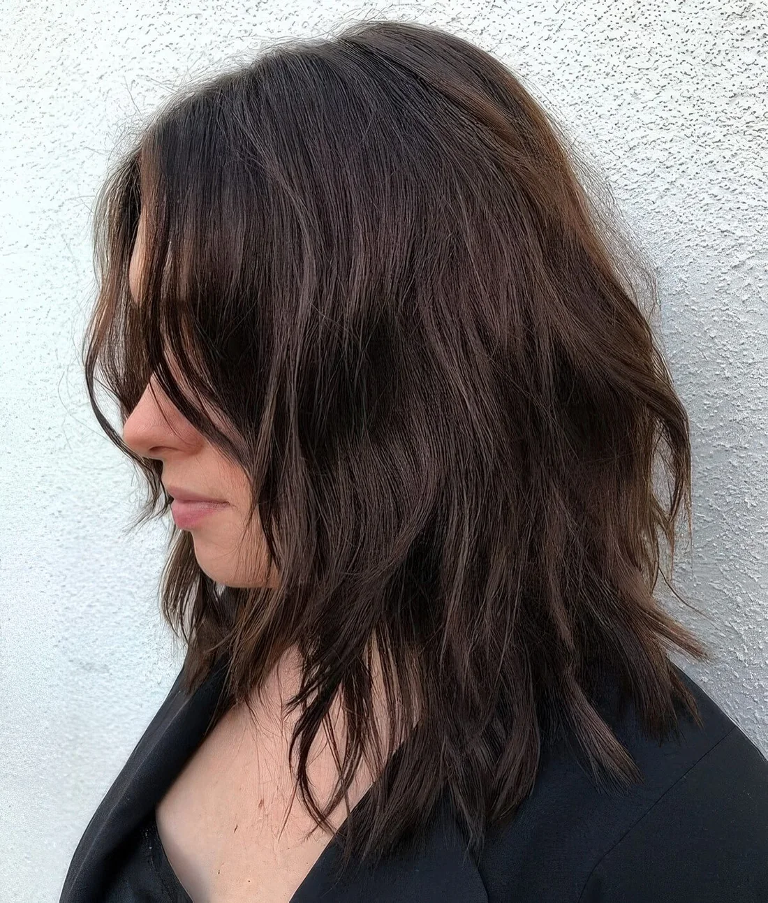 Dark brown choppy medium haircut with side bangs and messy waves shows off some texture and dimension.