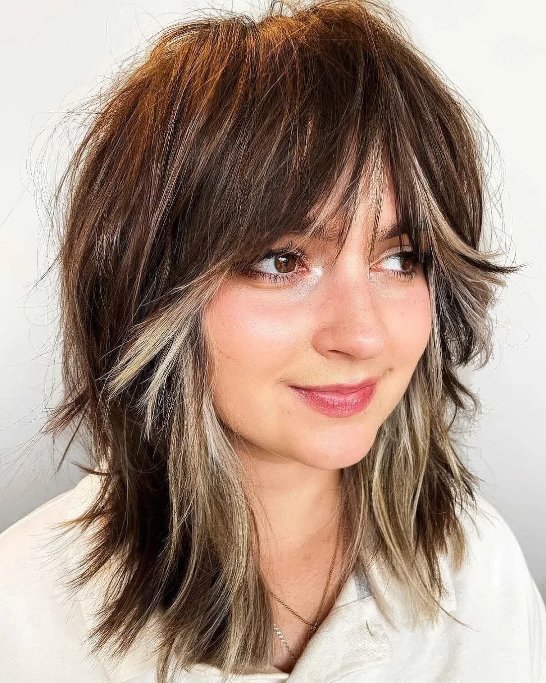 Layered shaggy haircut with blonde highlights and curtain bangs.