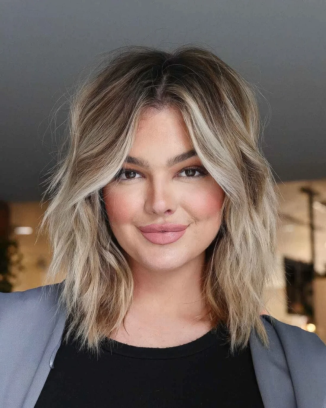 Medium layered and choppy haircut with blonde balayage and waves.