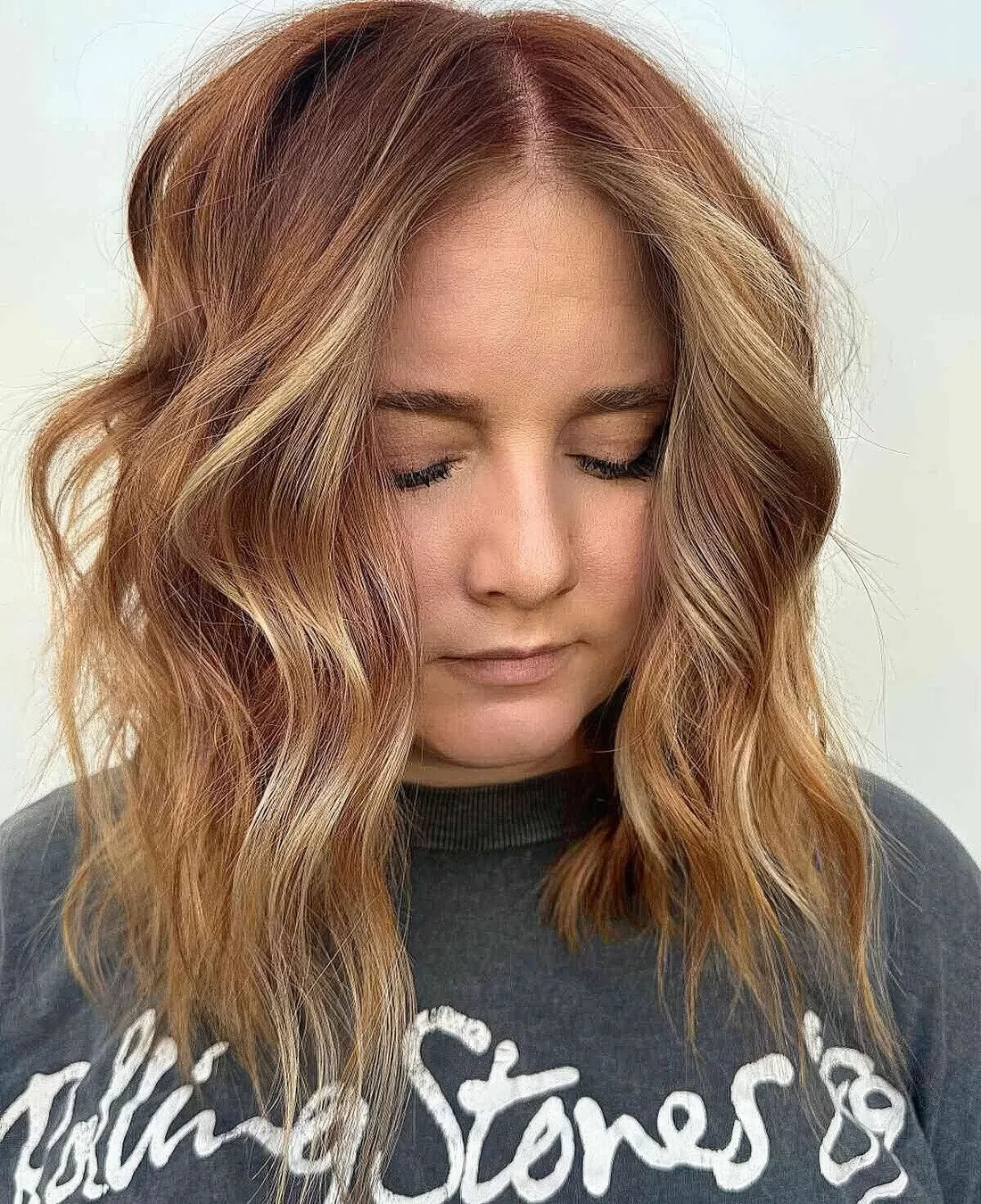 Medium-length hairstyle in a ginger shade and golden blonde highlights, with choppy layers and waves that feature texture.