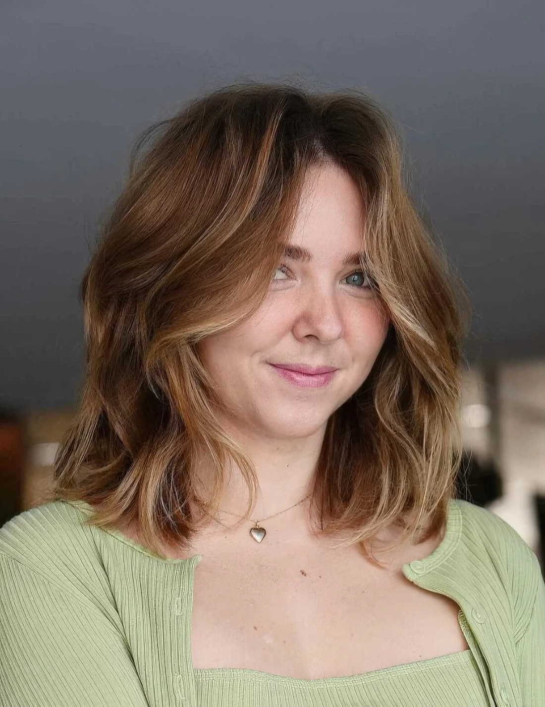Soft brown lob with blonde highlights and a lot of volume plus curtain bangs.
