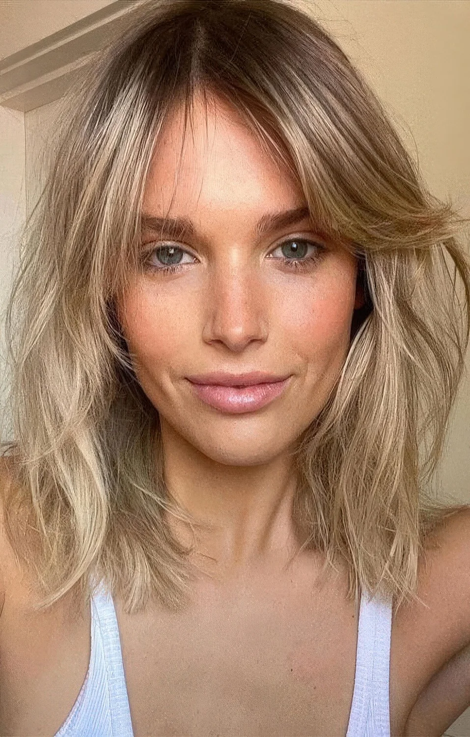 Blonde medium-length hairstyle with curtain bangs and messy volume.