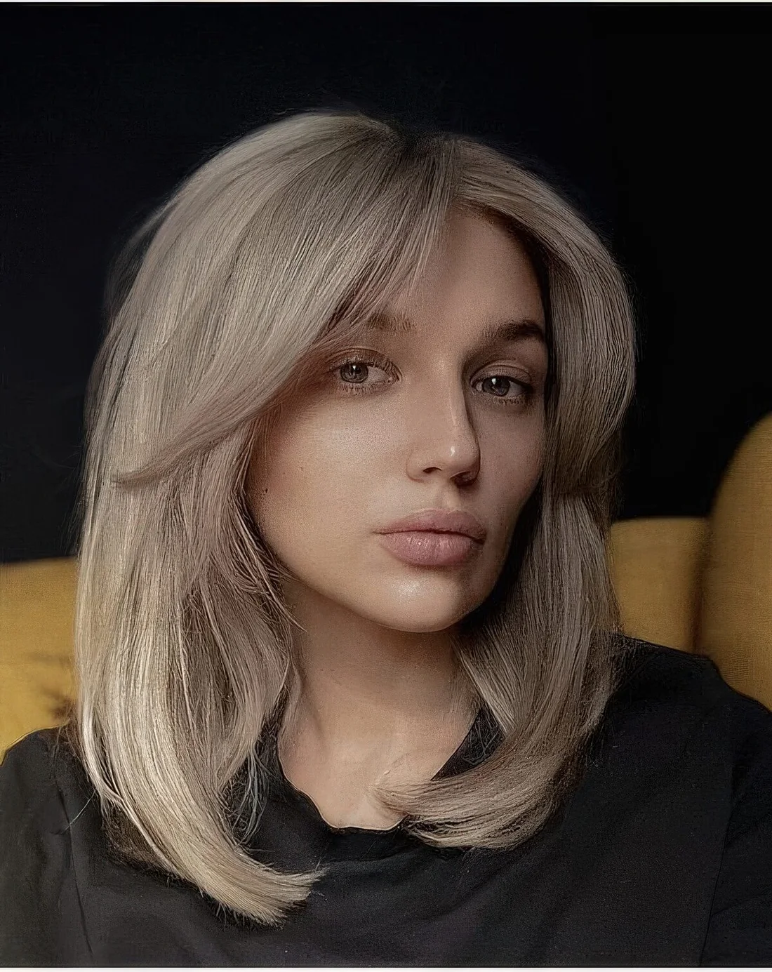 Blonde shoulder-length hairstyle with a lot of volume and curtain bangs.