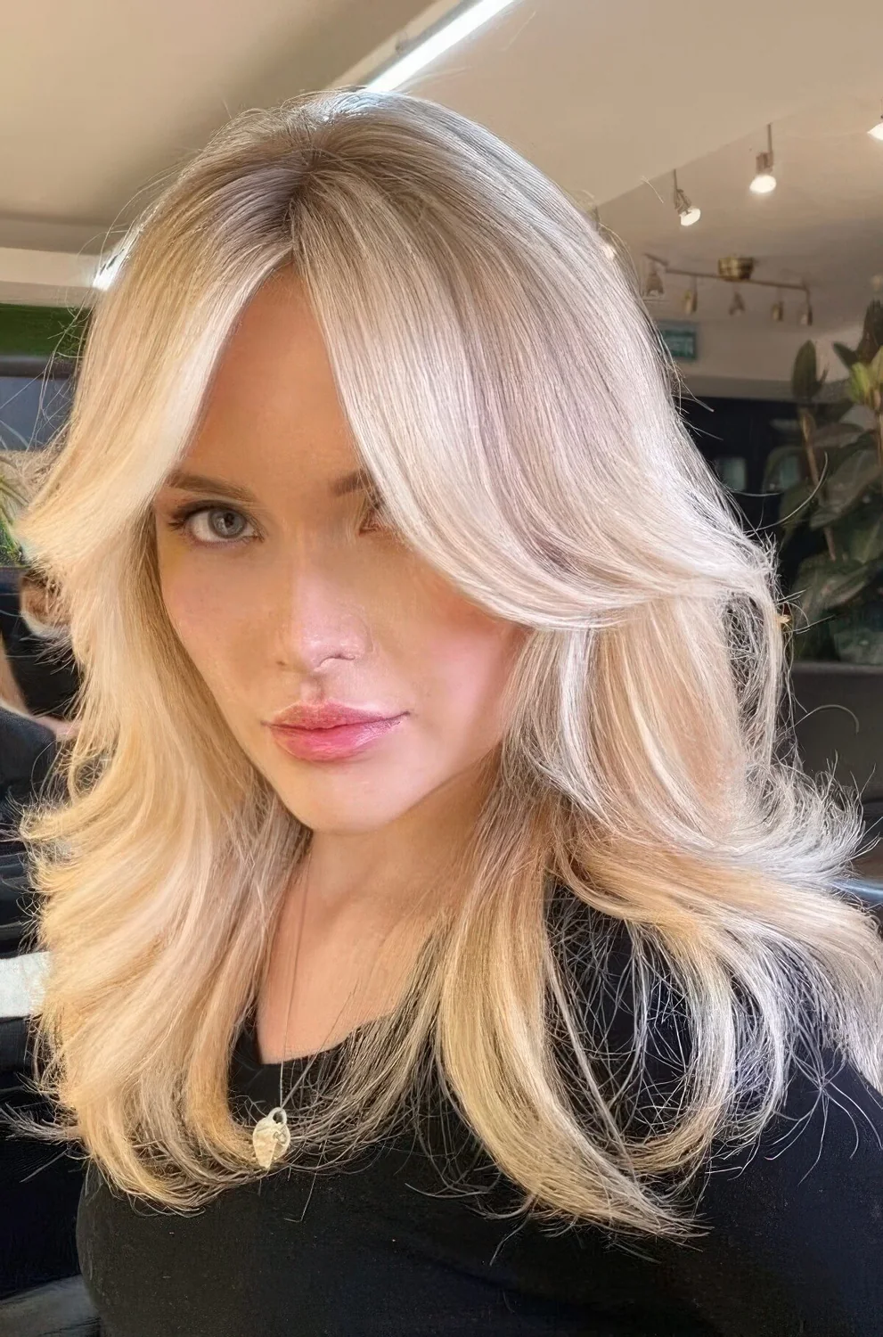Bright blonde butterfly haircut with wavy ends and a bit of volume, with curtain bangs.