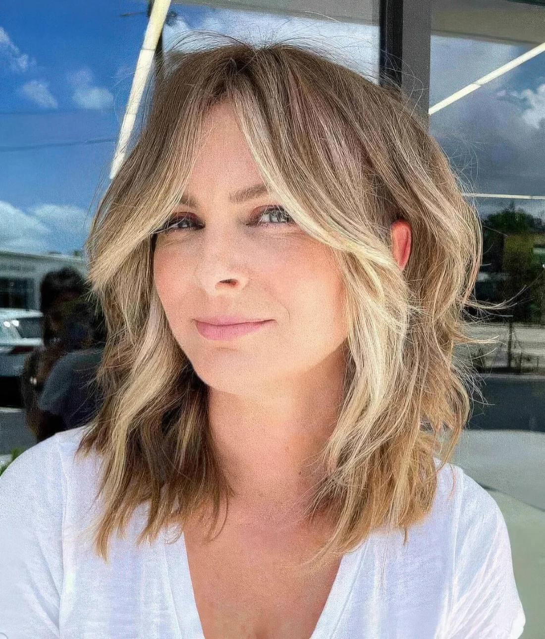Flattering face-framing wavy lob with curtain bangs and blonde highlights and money piece.
