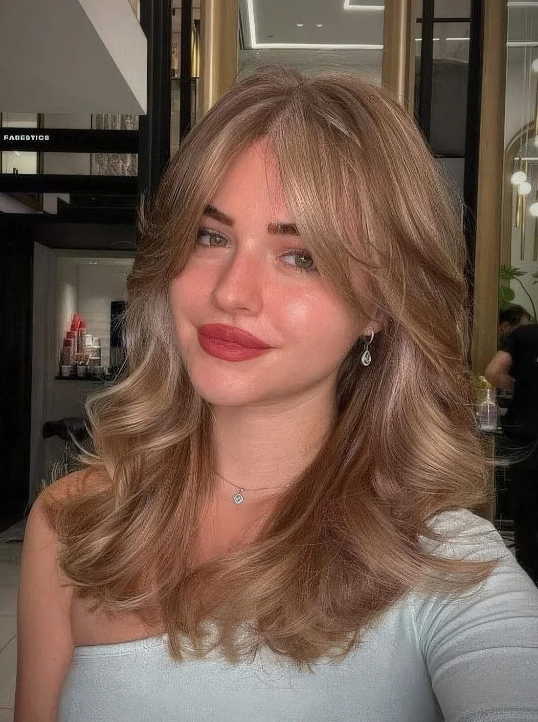 Bronde wavy hairstyle done on a butterfly haircut, with curtain bangs.