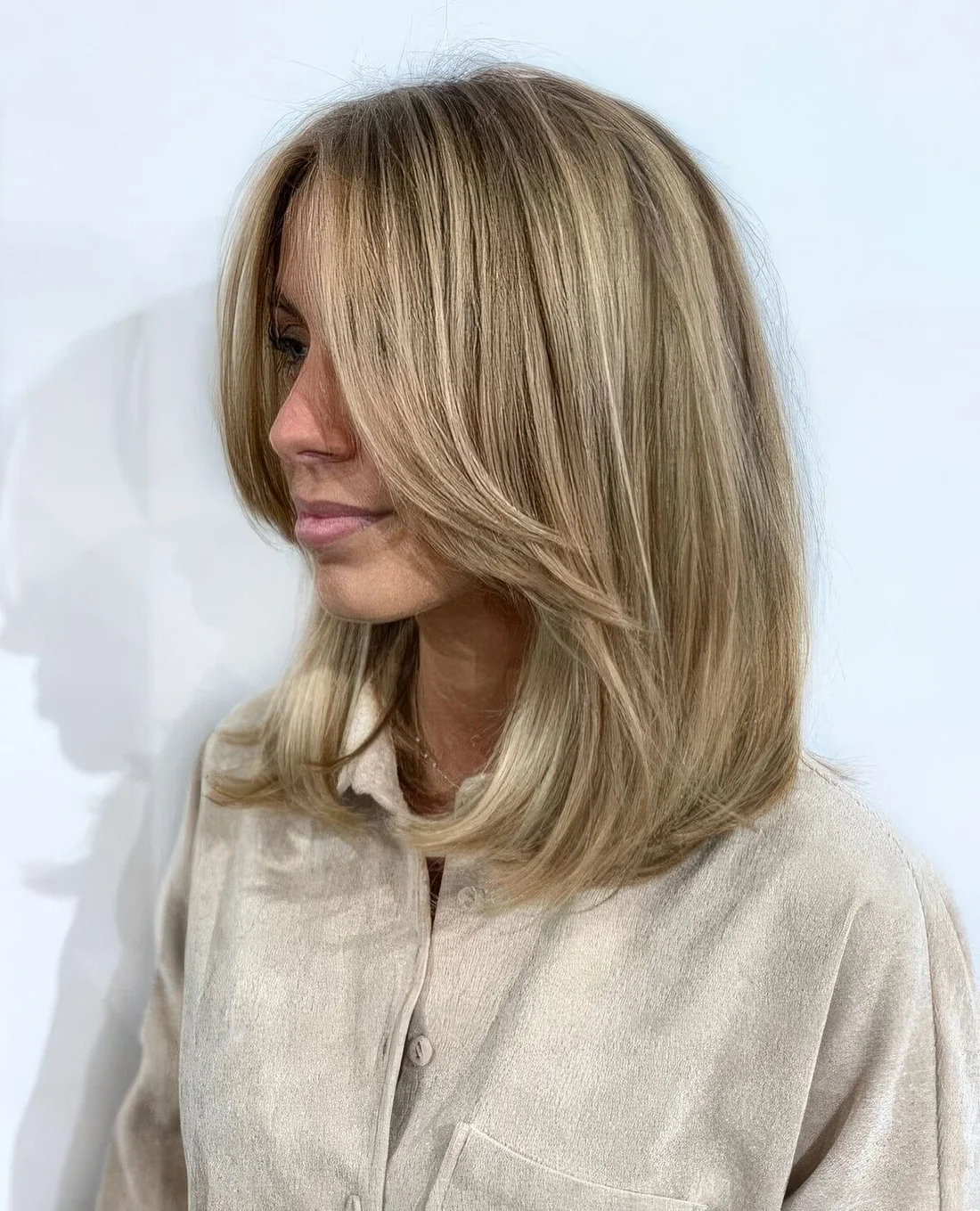 Medium-length blonde hairstyle with long curtain bangs and blonde balayage.