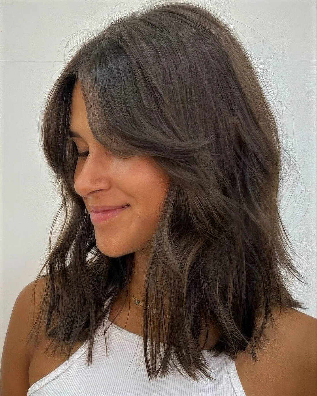 Medium-length shaggy dark brunette hairstyle with curtain bangs and a bit of volume.