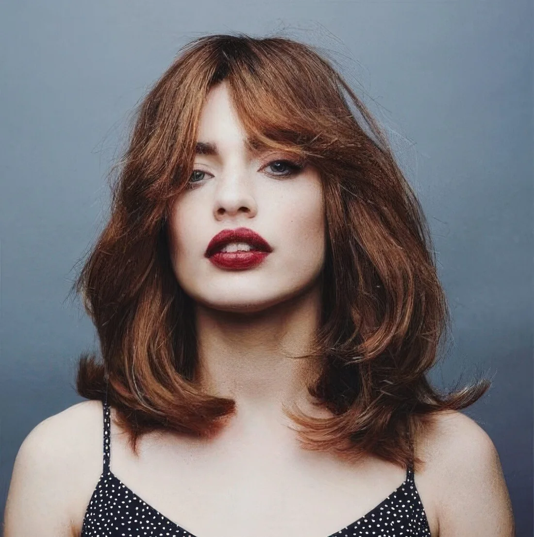 Shaggy layered medium haircut with curtain bangs and a beautiful ginger shade.