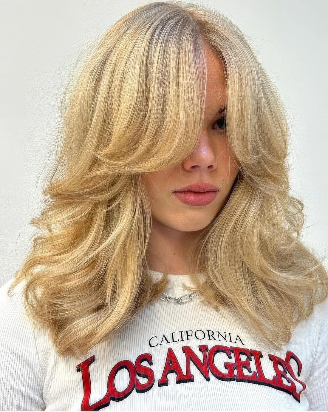 Blonde butterfly haircut with curtain bangs and wavy ends plus a lot of volume.