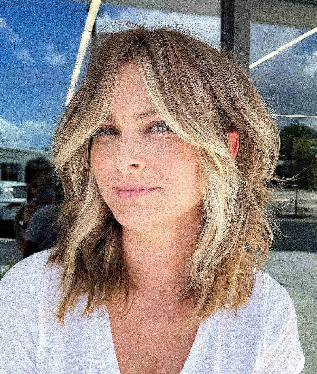 Flattering face-framing wavy lob with curtain bangs and blonde highlights and money piece.
