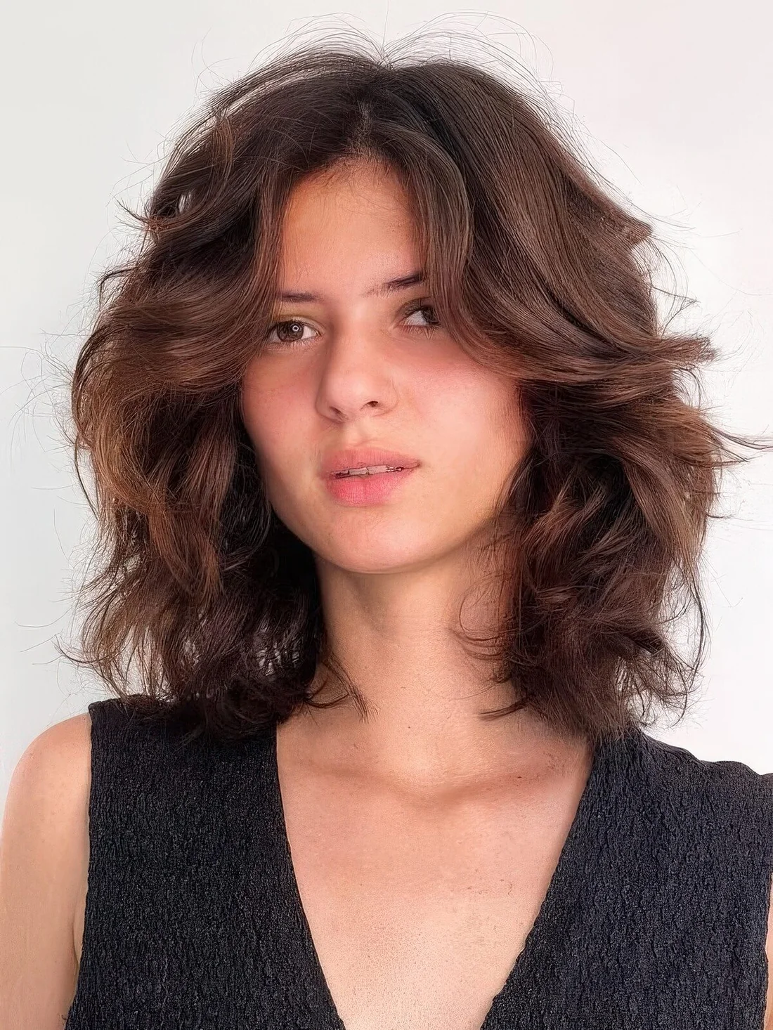 Dark brunette medium-length butterfly haircut on wavy hair, with a lot of dimension.