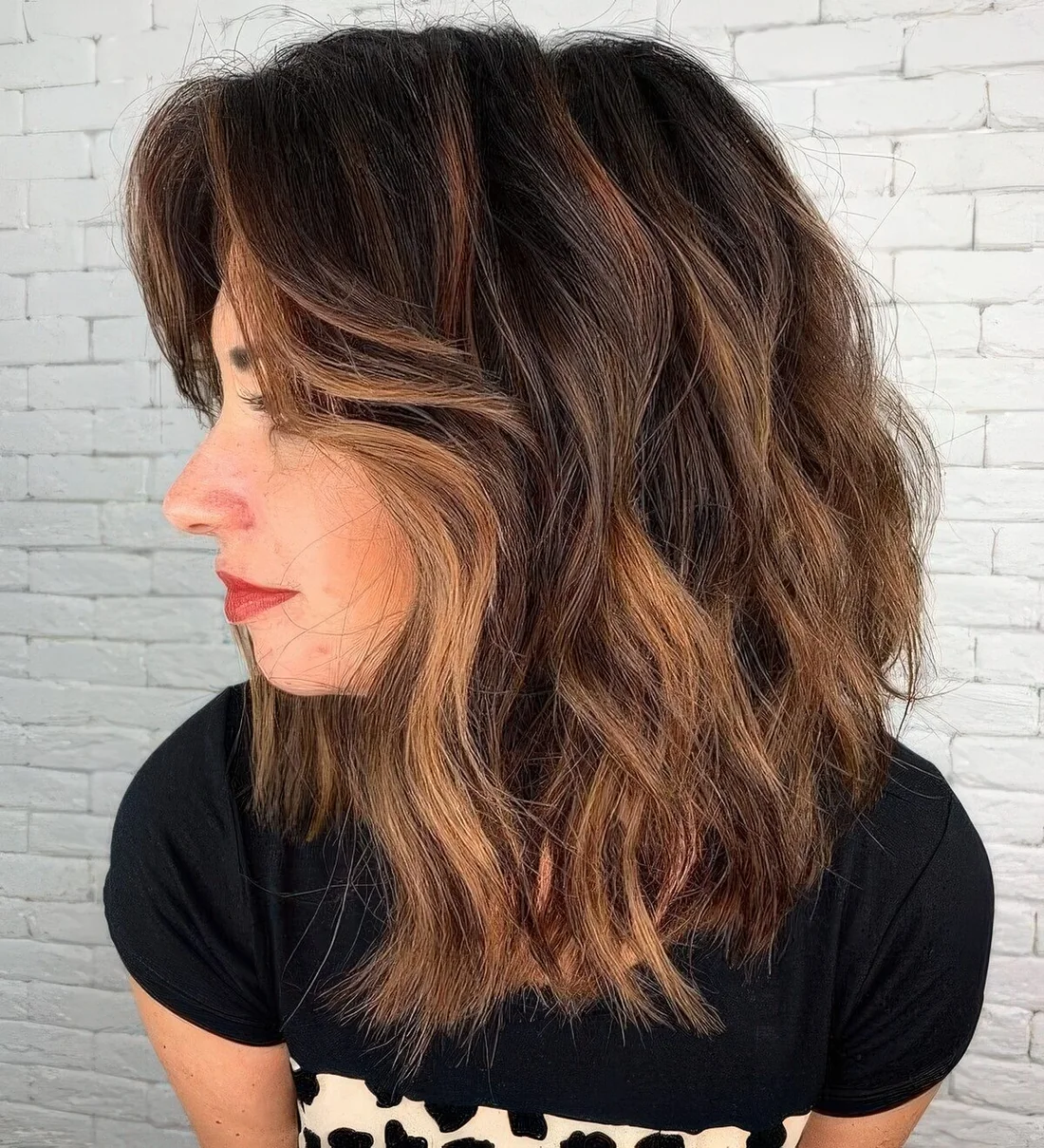 Black medium-length haircut with caramel balayage and waves, with side bangs.