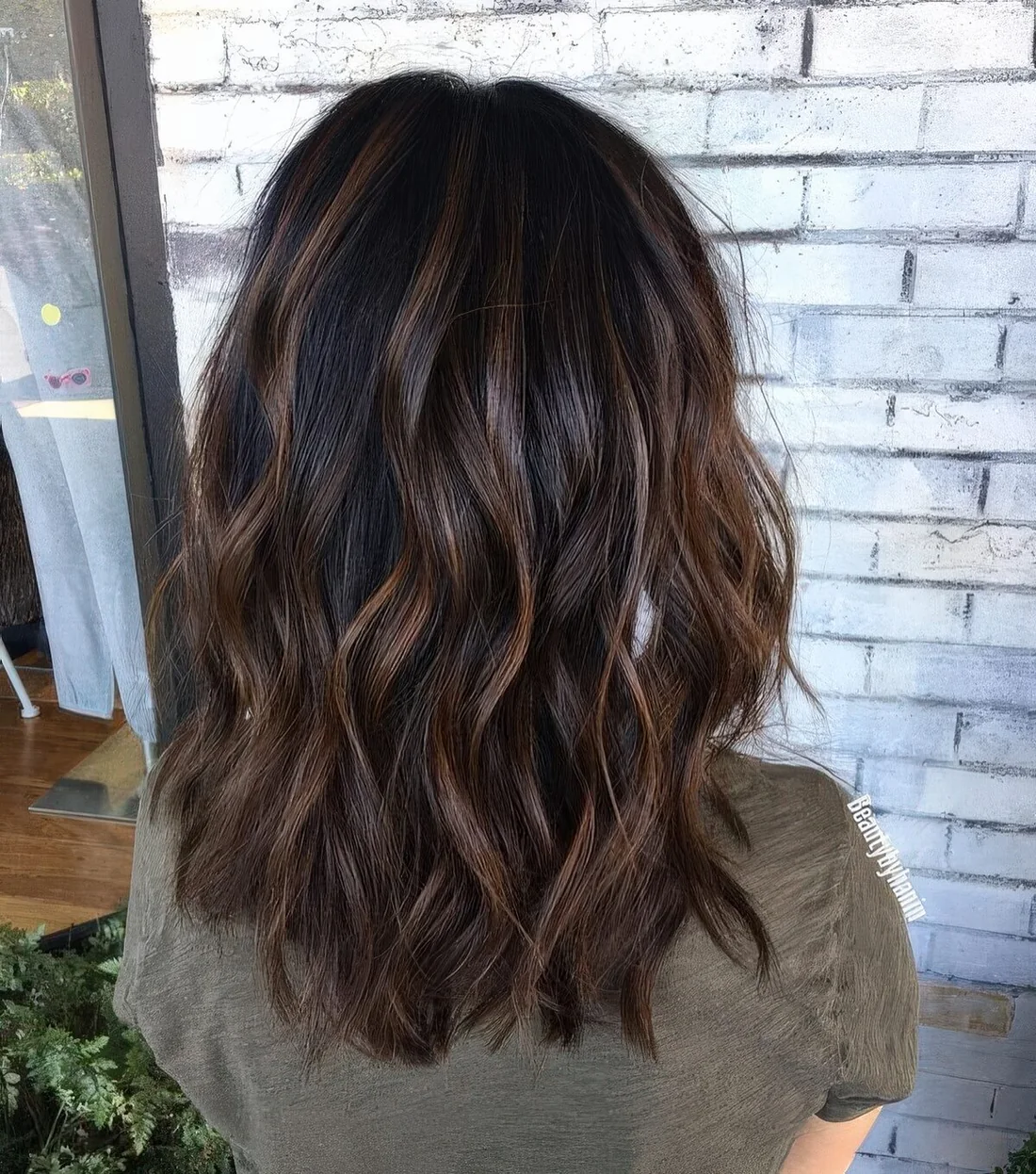 Black medium-length wavy hairstyle with caramel highlights and waves.