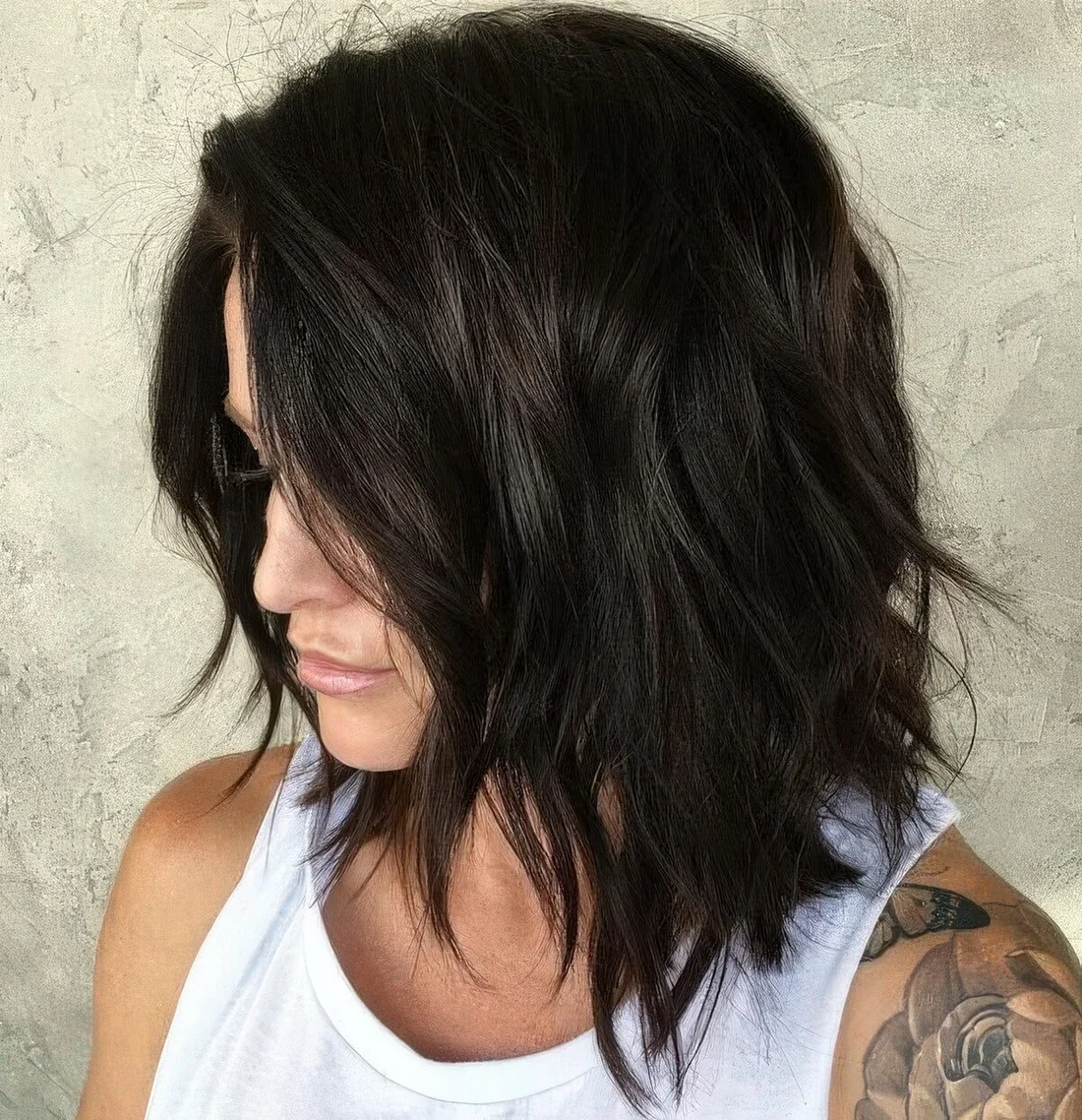 Black shaggy and choppy medium-length haircut with side part and messy waves.