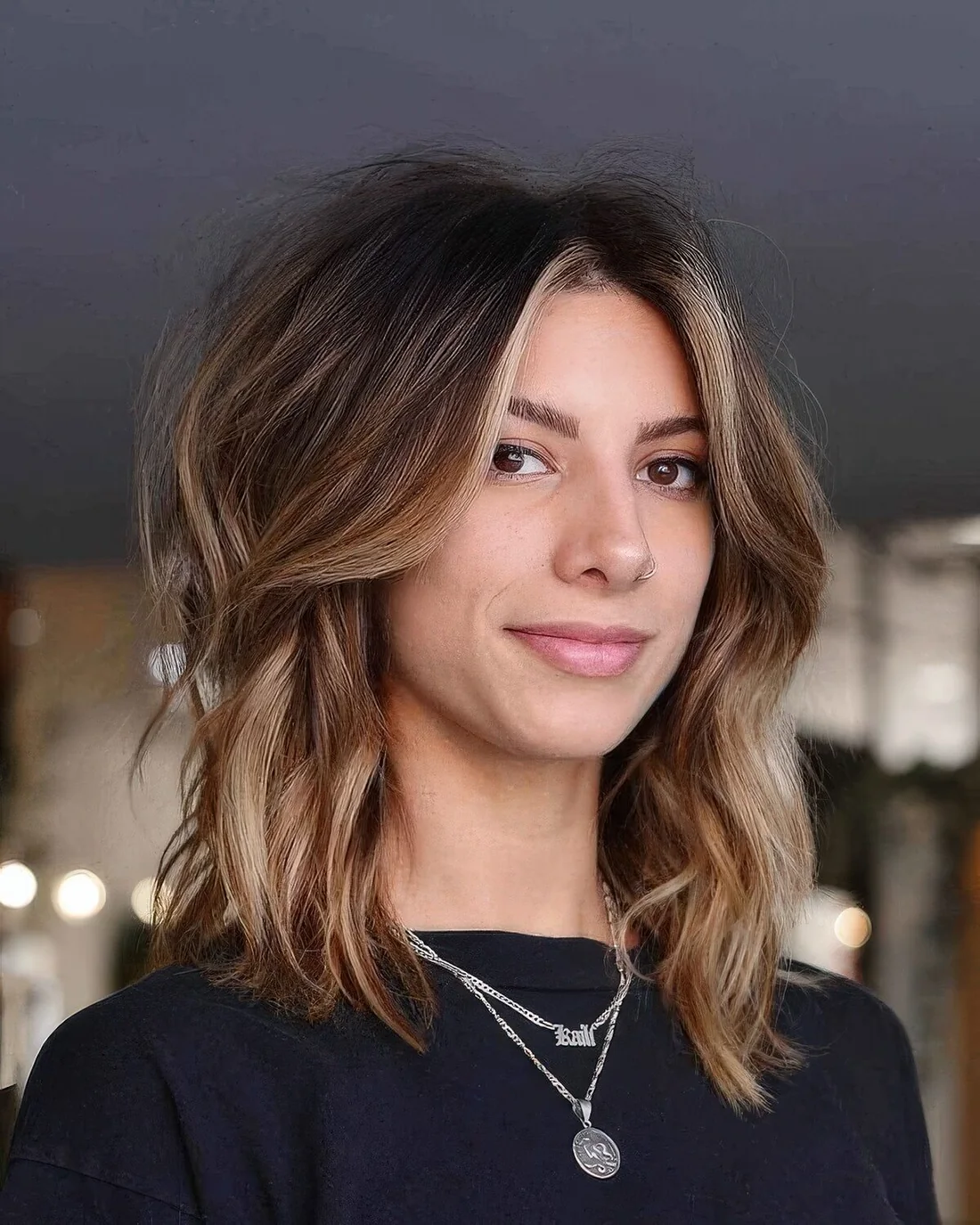 Brown medium-length haircut with blonde highlights, waves and side bangs that are made blonde.