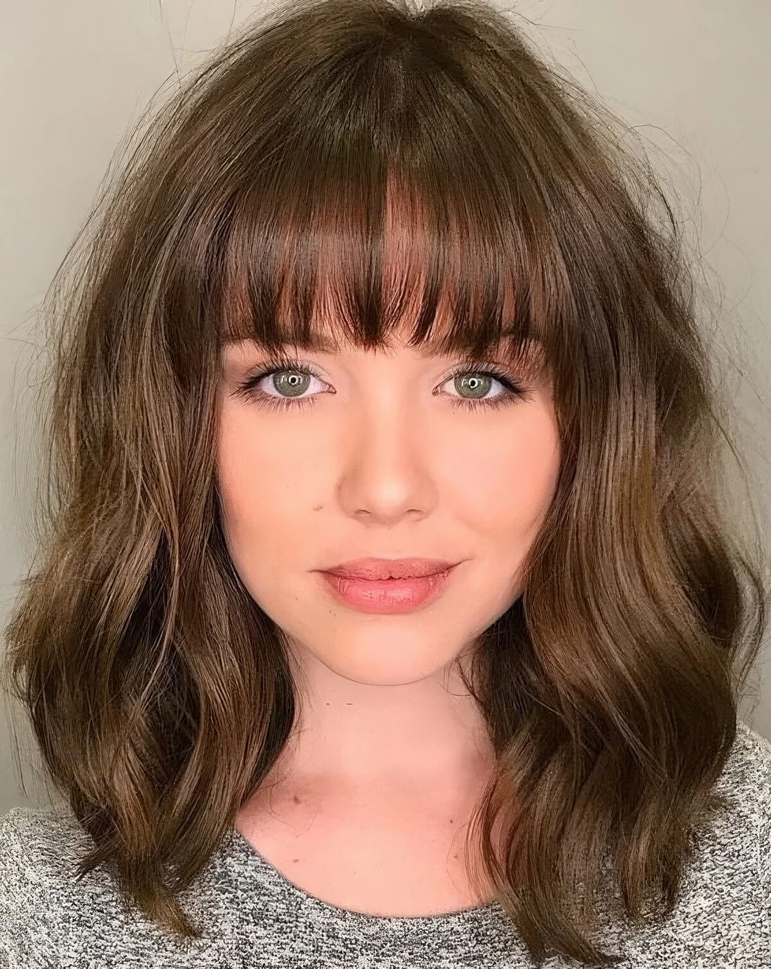 Brown medium-length wavy hairstyle with blunt bangs.