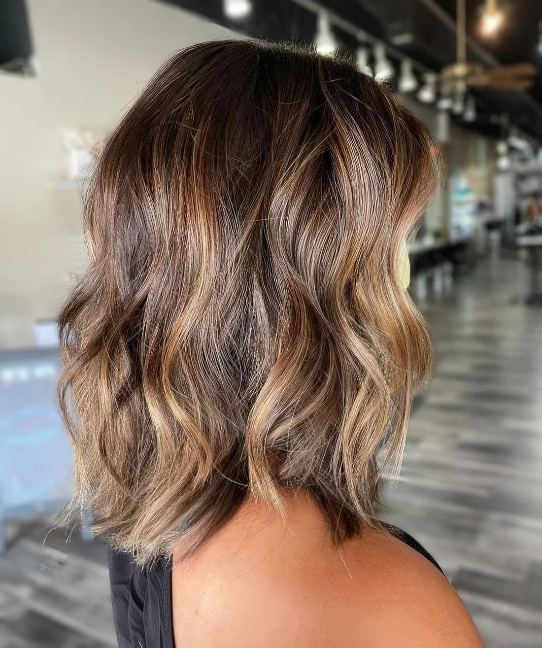 Brunette shoulder-length wavy hairstyle with caramel highlights.