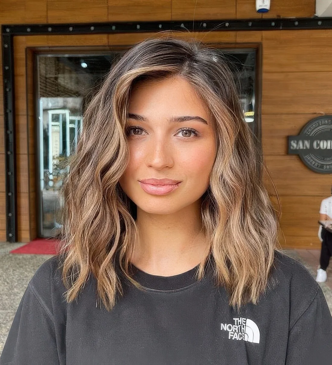 Chic brunette medium-length hairstyle with caramel balayage and waves down.